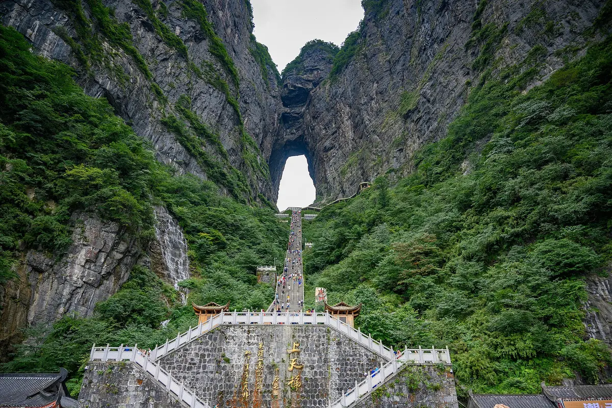 Heaven's Gate on Tianmen Mountain: a tall natural arch high in a sheer green cliff, with a long staircase of visitors climbing towards it